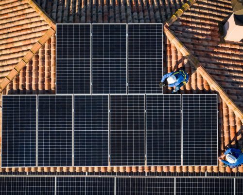 aerial view of Two workers installing solar panels on a house roof